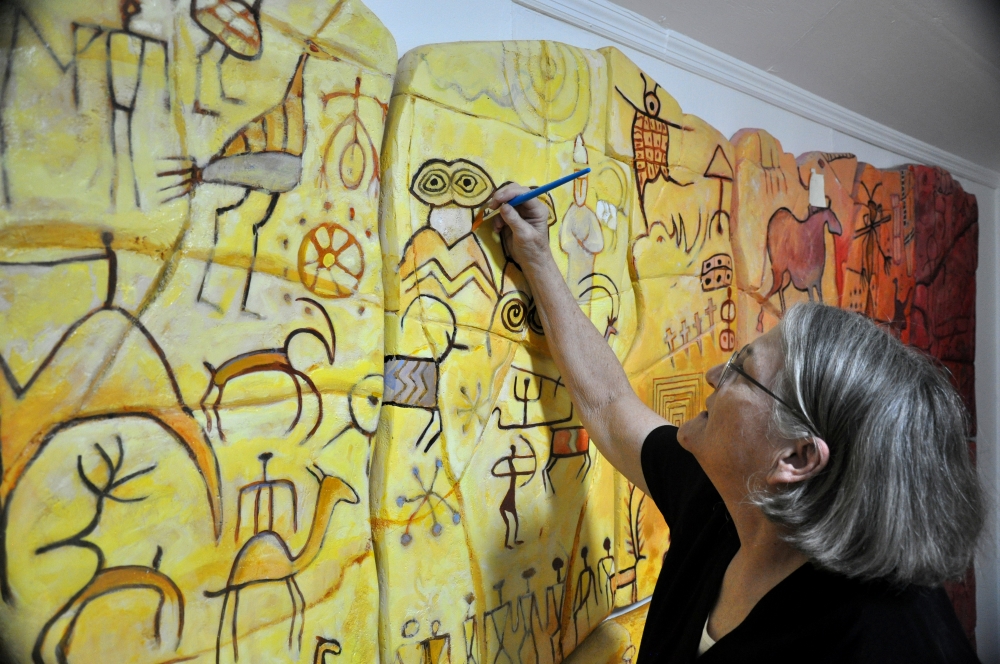Artist Cindy Rashe painting artworks with yellow, orange, red and browns to reveal historical markings and pictographs.